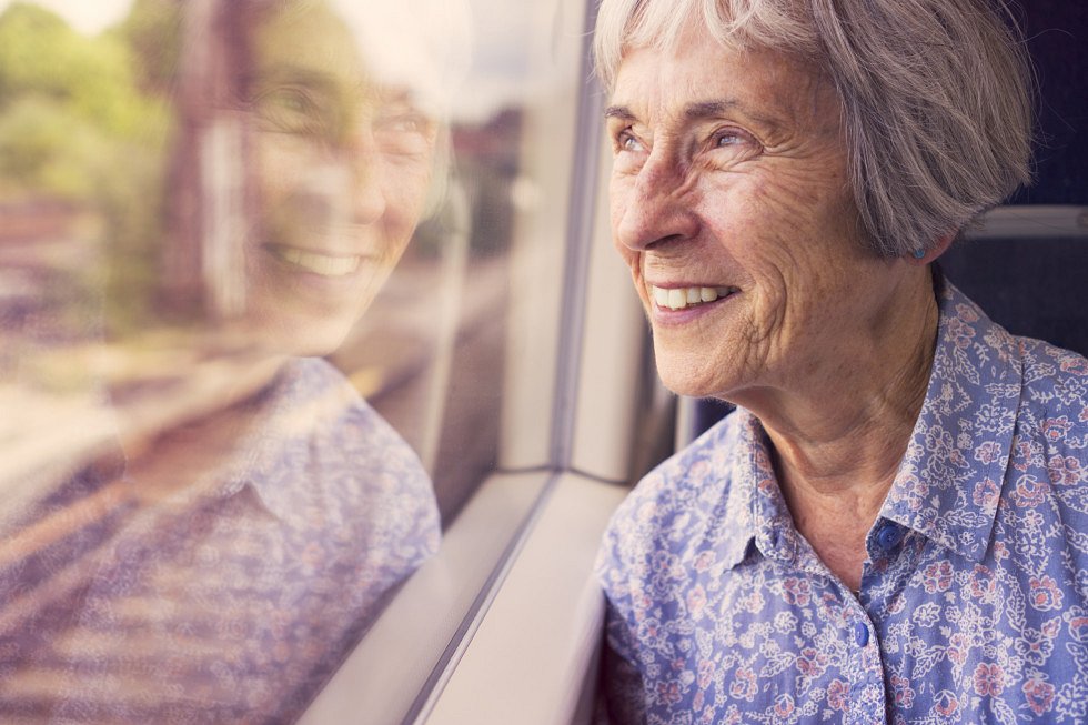Starejša gospa gleda okolico skozi okno vlaka