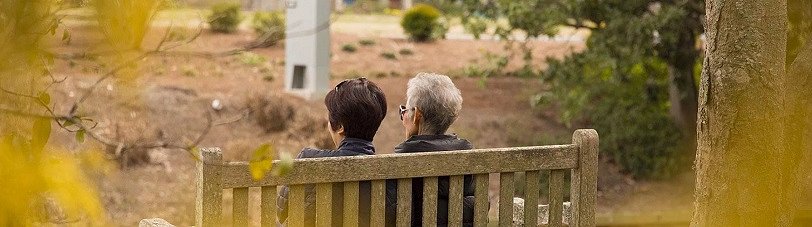 Na fotografiji sta dve starejši gospe, ki sedita na klopci v parku