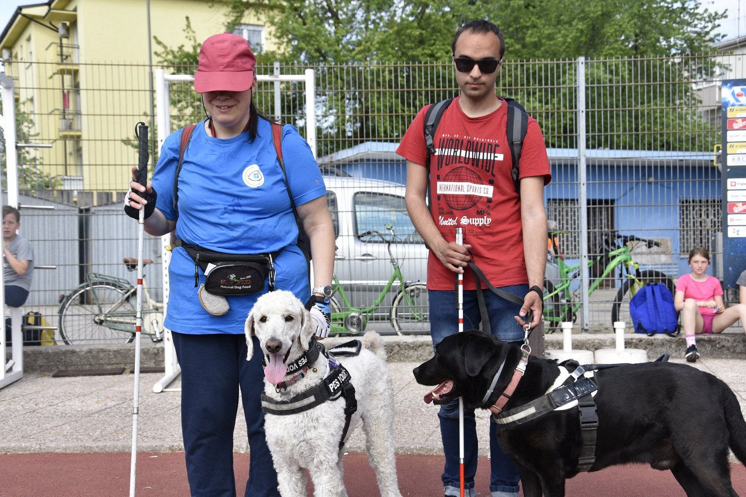 Slepi osebi stojita poleg svojih psov vodnikov